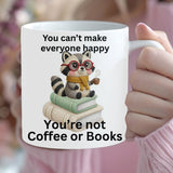 Person holding a mug with a raccoon illustration and text, surrounded by flowers.