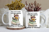 Two mugs with a raccoon illustration and humorous text, placed on a surface with decorative plants.