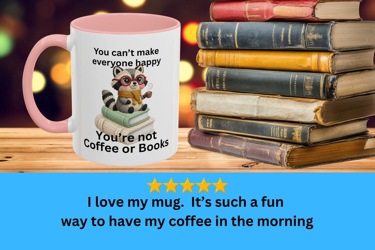 Mug with a raccoon illustration and text, placed on a stack of books with a blurred colorful background.