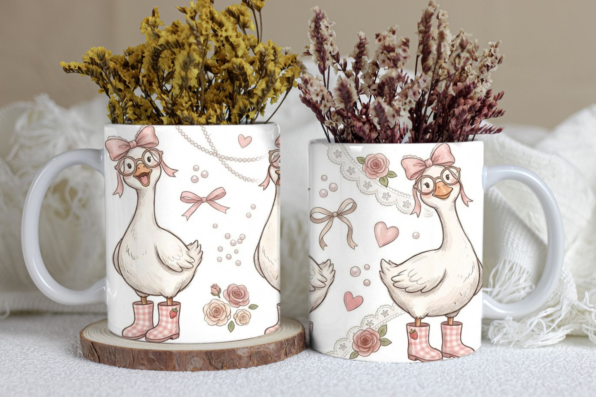 Two mugs with decorative designs of geese, flowers, and bows on a neutral background.