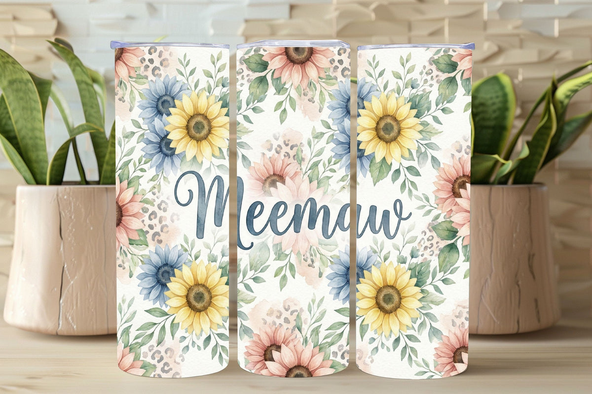 Three floral tumblers with 'Meemaw' text on a wooden surface with plants in the background.