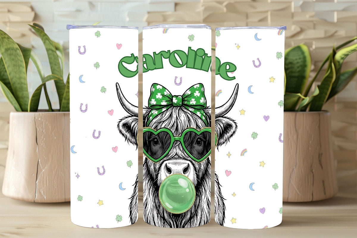 Tumbler with a cow design wearing sunglasses and a bow, with 'Caroline' text, on a wooden surface with plants.