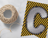 Decorative letter 'C' with yellow and black stripes next to a spool of twine on a light gray background