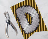 Metallic die-cut shape with a tool on a striped background