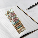 Floral and book-themed bookmark on an open notebook with a pen.