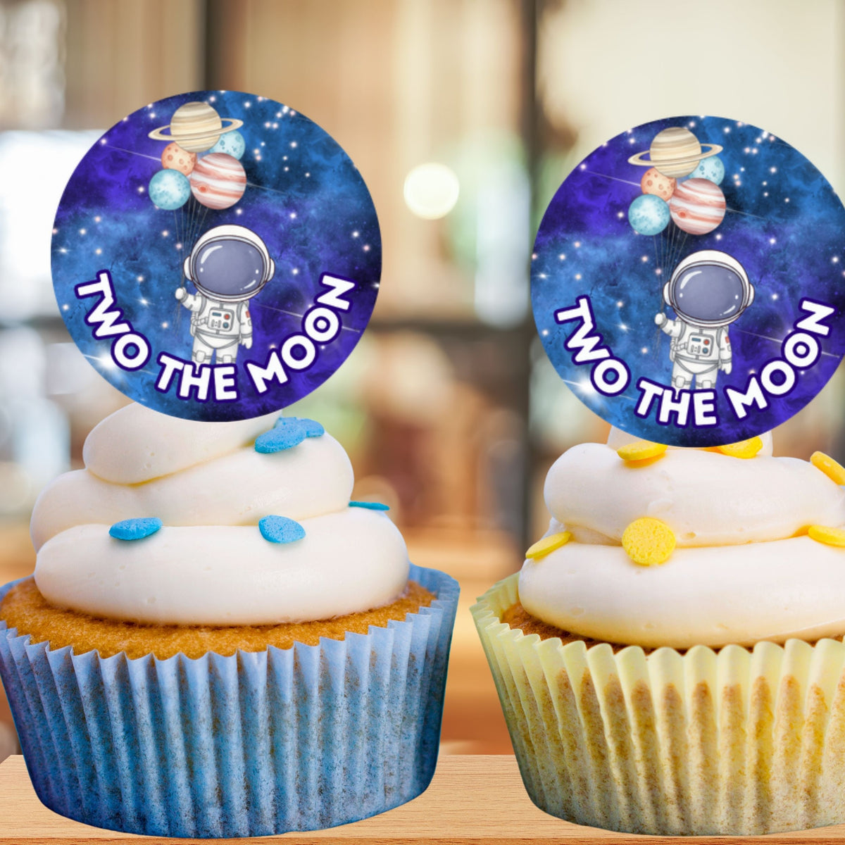 Two cupcakes with space-themed toppers featuring an astronaut and planets, labeled 'Two the Moon'.