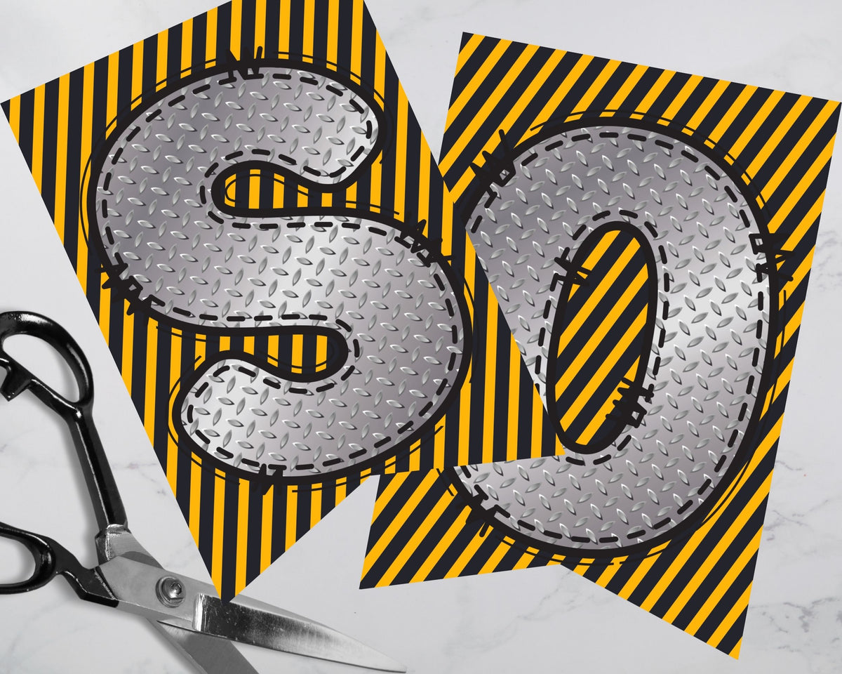 Two metallic letters 'S' and 'D' on yellow and black striped paper with scissors.