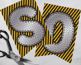 Two metallic letters 'S' and 'D' on yellow and black striped paper with scissors.