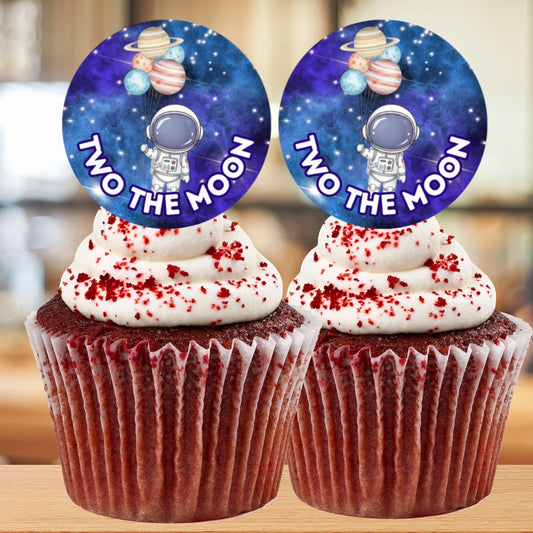 Two cupcakes with space-themed toppers labeled 'Two the Moon' on a blurred background.
