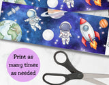 Space-themed paper with astronauts, rockets, and planets on a blue background with stars, scissors on a white surface.