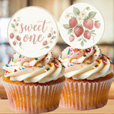 Two cupcakes with white frosting, colorful sprinkles, and 'sweet one' toppers on a wooden surface.