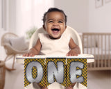 Baby in a high chair with a 'ONE' sign in a home setting
