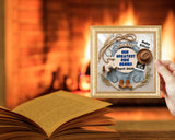 Framed baby announcement with cowboy theme held over an open book in front of a fireplace.