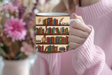 Person holding a mug with a bookshelf design, surrounded by flowers.