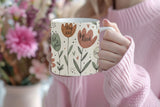 Person holding a mug with floral design and motivational phrases, blurred flowers in the background