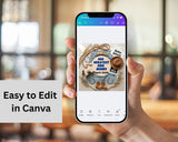 Hand holding a phone displaying a baby shower invitation design on Canva with blurred indoor background.