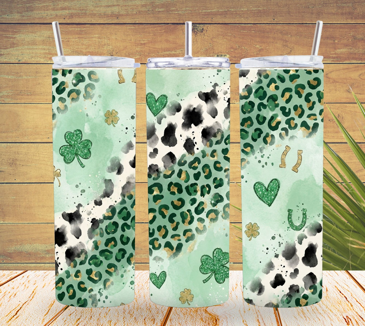 Three green patterned tumblers with straws on a wooden surface