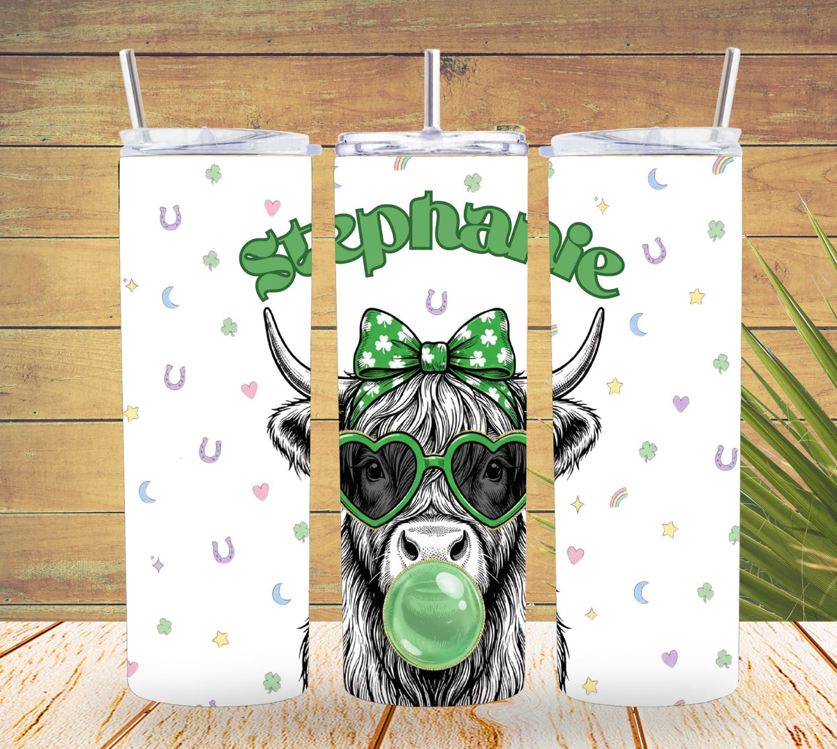 Three tumbler with straw designs featuring a cow with a bow and sunglasses on a wooden background.